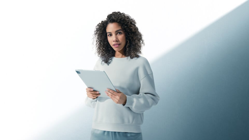 Una donna tiene in mano un tablet grigio davanti a uno sfondo grigio e bianco