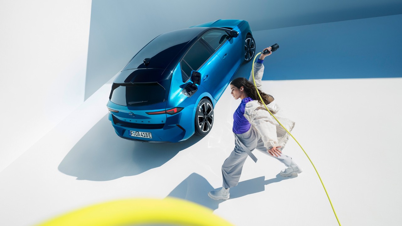 Vista dall'alto di una donna che regge il cavo di ricarica di fianco a una Opel Astra Electric blu