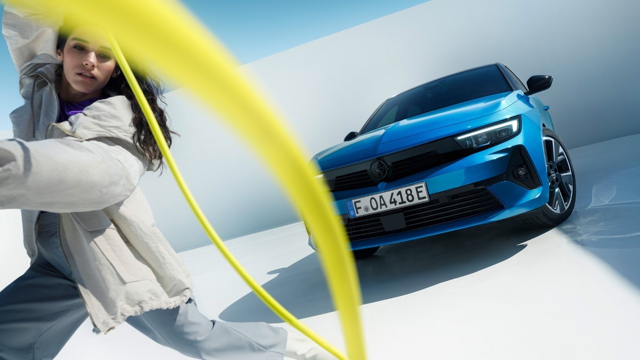 Una donna regge il cavo di ricarica davanti a una Opel Astra Electric blu