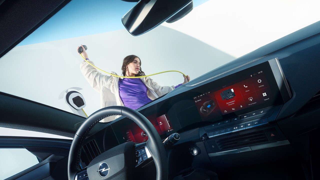 Primo piano dell'interno di una Opel Astra Sports Tourer Electric con una donna che tiene il cavo di ricarica EV all'esterno