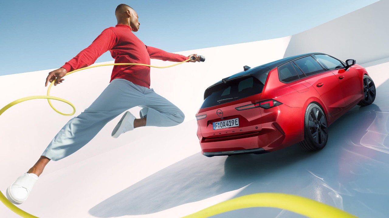 Un uomo salta con un cavo di ricarica EV con alle spalle una Opel Astra Sports Tourer Electric