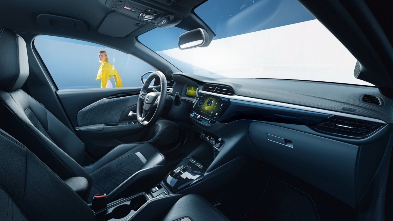 Vista laterale dell'interno nero di Opel Corsa Electric vista dal sedile del passeggero con una donna sullo sfondo 