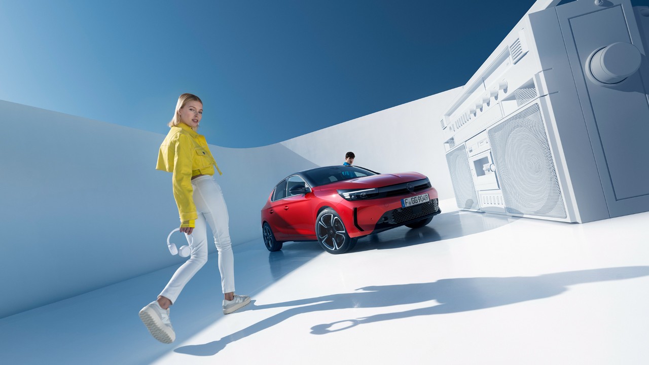 Donna in piedi accanto alla nuova Opel Corsa di colore rosso con tetto nero e un uomo che sale dalla portiera del guidatore